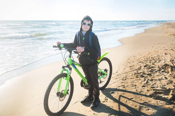 Niño monta una bicicleta a lo largo del mar en una playa de arena . —  Fotos de Stock