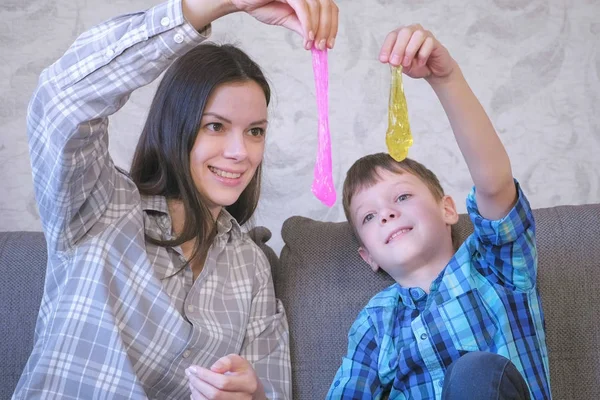 Feliz mamá y su hijo están jugando con el limo sentado en el sofá. Baba de estirar . — Foto de Stock