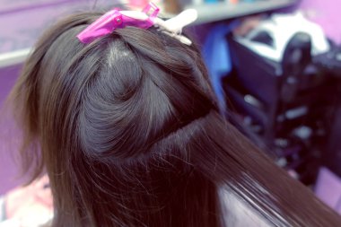 Kuaför düzlüklerde koyu kumral saç maşa güzellik salonunda kullanarak kadının. Saç yakın çekim.