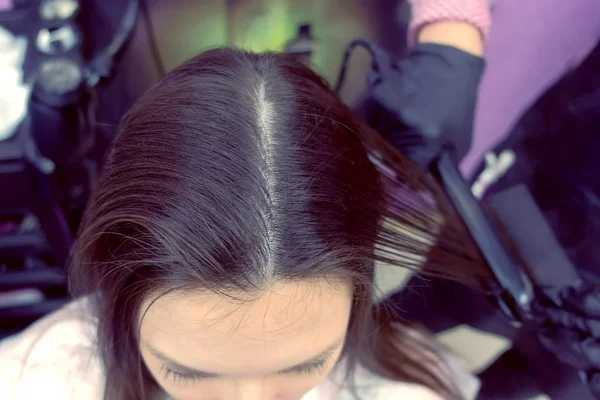 Friseur glättet dunkelbraune Haare der schönen Frau mit einer Haarzange im Schönheitssalon. Ansicht von oben. — Stockfoto