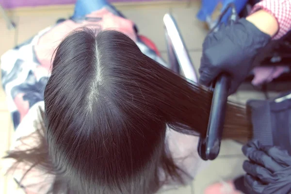 Парикмахер прямые темные каштановые волосы красивой женщины, используя щипцы для волос в салоне красоты. Вид сзади . — стоковое фото