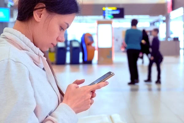 Mulher check-in inscrição on-line em seu telefone celular no hall do aeroporto, vista lateral . — Fotografia de Stock