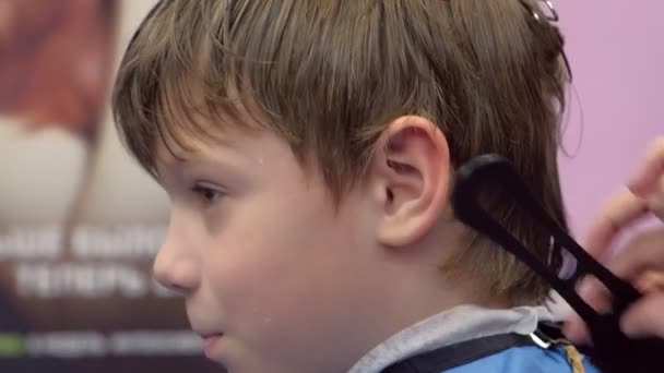 Niño en una peluquería para un corte de pelo, cara de cerca, vista lateral . — Vídeos de Stock