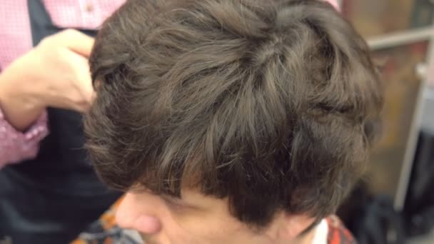 Перукар розрізає волосся за допомогою затискача на голові чоловіка. Вид зверху, стилісти руки крупним планом . — стокове відео