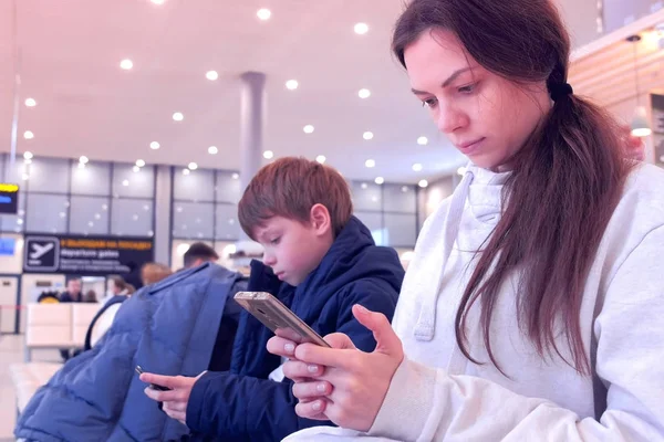 Frau mit ihrem Sohn surft auf Mobiltelefonen in Flughafenhalle und wartet auf Flug. — Stockfoto