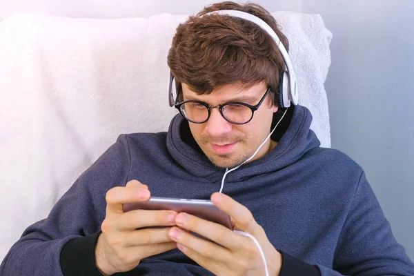 Чоловік в окулярах і навушниках грає в гру в смартфоні. Гамер розслабляється . — стокове фото