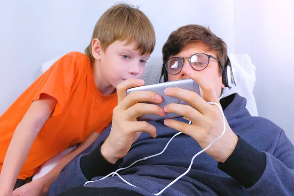 Mann mit Brille und Kopfhörer spielt mit seinem Sohn ein Spiel im Smartphone. Spieler entspannen. — Stockfoto