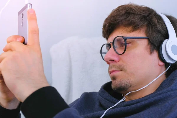 Чоловік в окулярах і навушниках дивиться відео на мобільний телефон. Вид збоку . — стокове фото