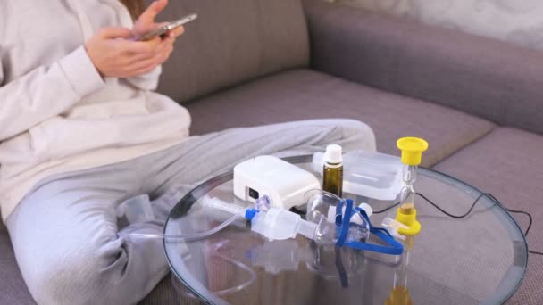 Preparación para inhalación. Nebulizador, mascarilla y medicina en la mesa de cristal. Mujer irreconocible con teléfono móvil . — Vídeo de stock