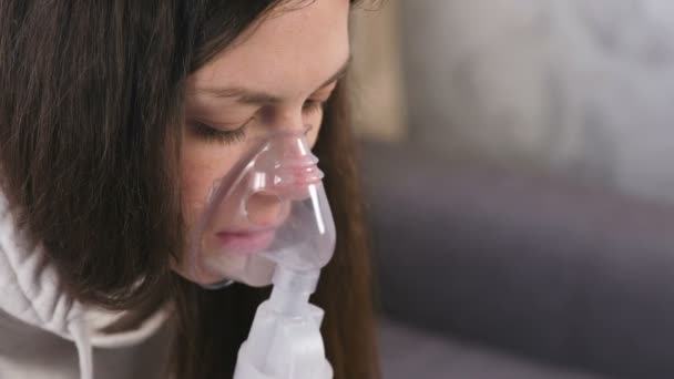 Use nebulizador e inhalador para el tratamiento. Mujer joven inhalando a través de la máscara del inhalador. Cara de cerca, vista lateral . — Vídeo de stock