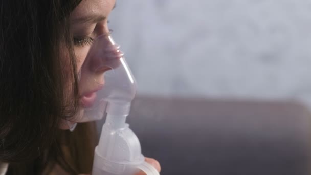 Use nebulizador e inhalador para el tratamiento. Mujer joven inhalando a través de la máscara del inhalador. Cara de cerca, vista lateral . — Vídeos de Stock