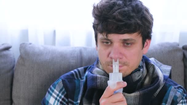 Homem doente inalando através do bocal inalador para o nariz sentado no sofá. Cara de perto, vista frontal. Use nebulizador e inalador para o tratamento . — Vídeo de Stock