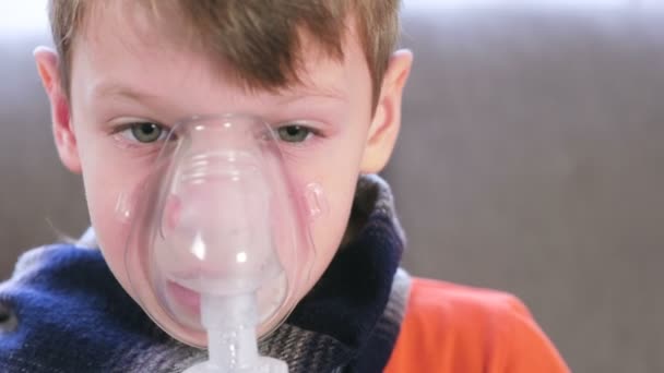 Sjukt blond pojke andas in genom inhalatorn mask, närbild ansikte. Använda nebulisatorn och inhalator för behandling. — Stockvideo