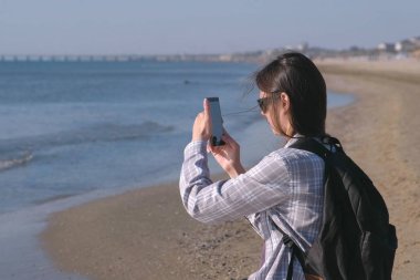 Kumlu deniz plaj ve fotoğraf ve video üstünde hareket eden telefon yapım sırt çantası blogger'da kızla gezgin.