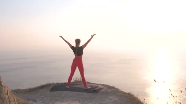 Hermosa vista de mujer haciendo yoga estirándose en la montaña con vista al mar al atardecer. Brazos de estiramiento . — Vídeo de stock