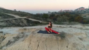 Güzel kadın yoga stretcing gün batımında deniz manzaralı dağ tepesinde yapıyor. Havadan görüntüleri.