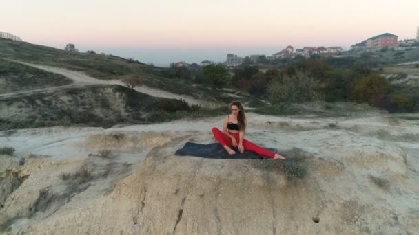Güzel kadın yoga stretcing gün batımında deniz manzaralı dağ tepesinde yapıyor. Havadan görüntüleri. — Stok video