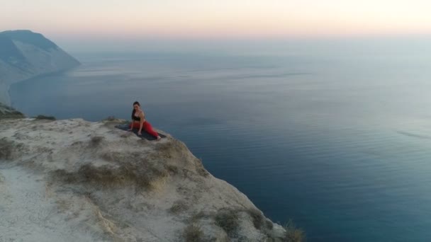 Vacker ung kvinna gör yoga restaurangtäta på toppen av berget med utsikt över havet vid solnedgången. Antenn material. — Stockvideo