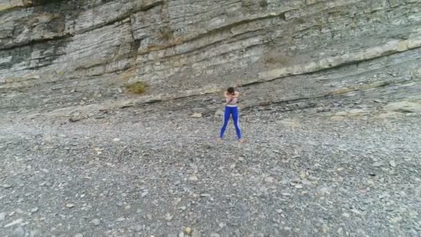 Vrouw doet yoga en fysieke oefeningen op rock en zee achtergrond. Luchtfoto mooi beeldmateriaal bekijken. — Stockvideo