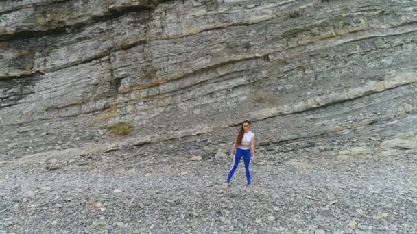 女性がスクワットをやっている岩と海の背景に bodyflex。空中の美しい映像表示. — ストック動画
