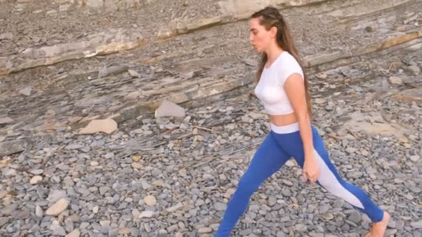 女孩做蹲冲刺身体弯曲在呼吸锻炼在岩石背景. — 图库视频影像