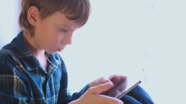 Çocuk pencere içinde oturan tablet oyun oynuyor.