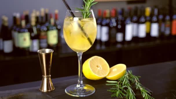 Cocktail alcolico con spumante, ghiaccio e liquore, limone e rosmarino in bicchiere da vino sul bancone del bar, vista da vicino . — Video Stock