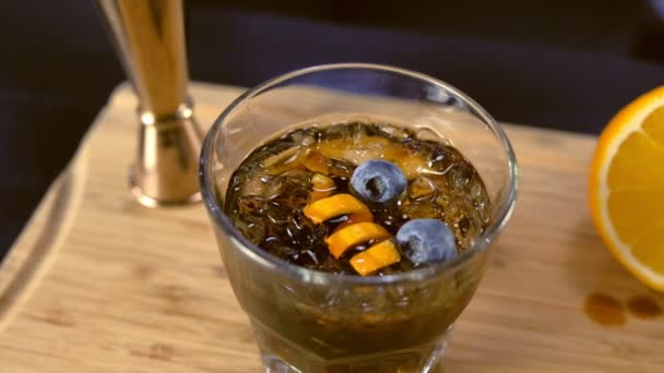Alkohol cocktail på stenar glas med apelsin, ice och blåbär på bordet, ovanifrån. — Stockvideo