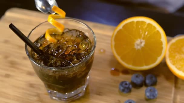 Barman zdobí koktejl alkoholu na skleněné kameny s Borůvka a orange zest. Rukou detail. — Stock video