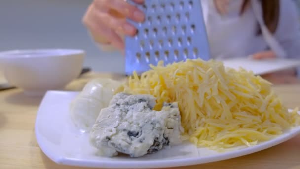 Woman puts rub cheese on grater on plate with different sort of cheese. Hands close-up. — Stock Video