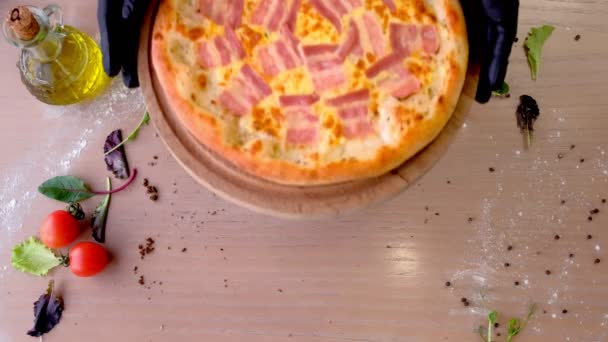 Šéfkuchař v gumové rukavice klade slanina pizzu na dřevěném prkénku na stole. Rukou detail. — Stock video