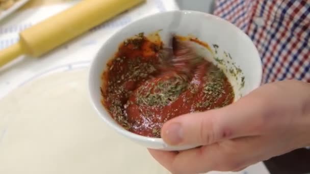 El hombre mezcla salsa de tomate con albahaca seca en un plato. Salsa para la pizza. Primer plano de las manos . — Vídeos de Stock