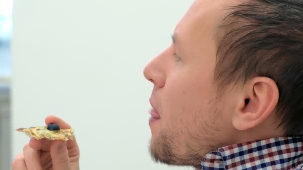 El hombre está comiendo una rebanada de pizza, vista lateral, cara de cerca . — Vídeos de Stock