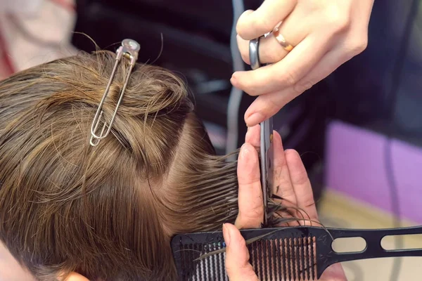 Hairdresser cutting hairs with scissors on boys head. Top view, stylists hands close-up.