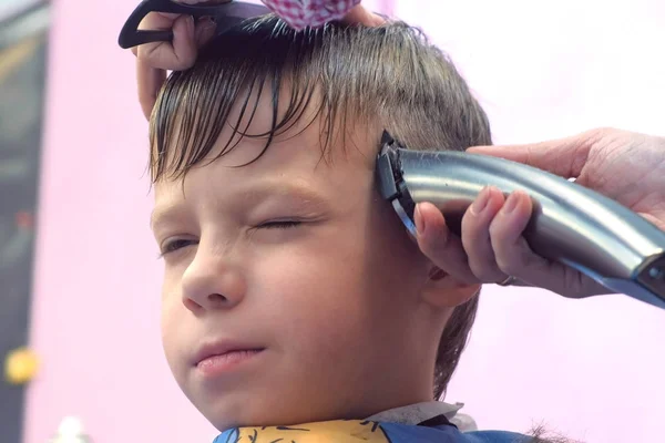 Hairdresser cuts hairs with clipper on boys head. Front view, stylists hands close-up. — Stock Photo, Image