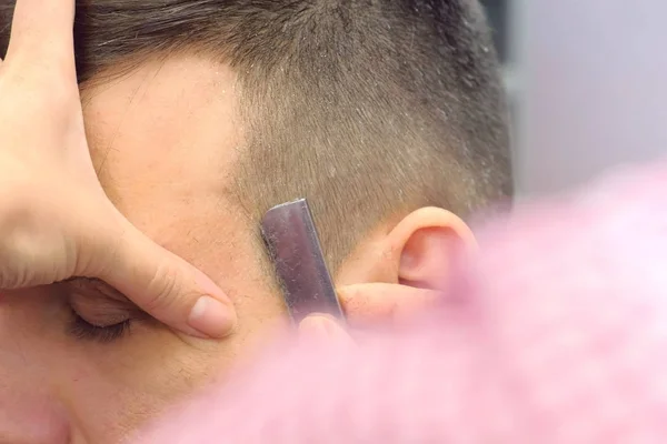 Парикмахер бреет волосы на висках мужчин острой бритвой. Стилисты разводят руками крупным планом. — стоковое фото