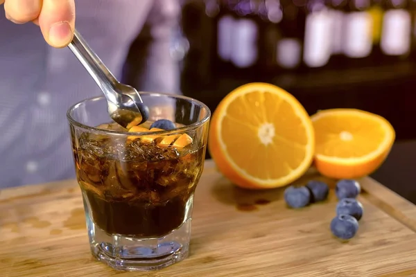 Barman zet blueberry in alcohol cocktail op het glas van de rotsen. Close-up van de handen. — Stockfoto