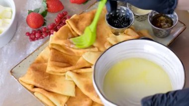 Cook yağlar yağ ile geleneksel Rus krep, blini. Lastik eldiven yakın çekim elinde. Reçel, ekşi krema, süt ve çilek plaka servis.