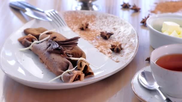 Chocolade Russische pannenkoeken, blini met wrongel invullen op de plaat. Geserveerd met een kopje thee en boter. Zijaanzicht. — Stockvideo