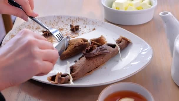 Woman, is eating chocolate russian pancakes, blini with curd filling on the plate. Hands close-up. Served with tea. Close-up hands, side view. — Stock Video