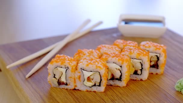 Rollos con pescado, camarones y caviar naranja en la parte superior servidos en tablero de madera con wasabi y salsa de soja . — Vídeos de Stock