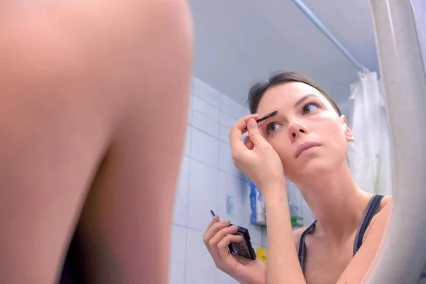美丽的黑发女人画眉毛在浴室在镜子前. — 图库照片