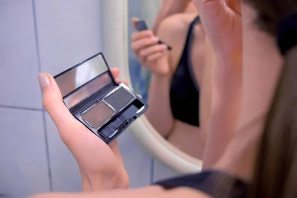 美しいブルネットの女性は、鏡の前で浴室の眉毛を描画します。背面図. — ストック写真