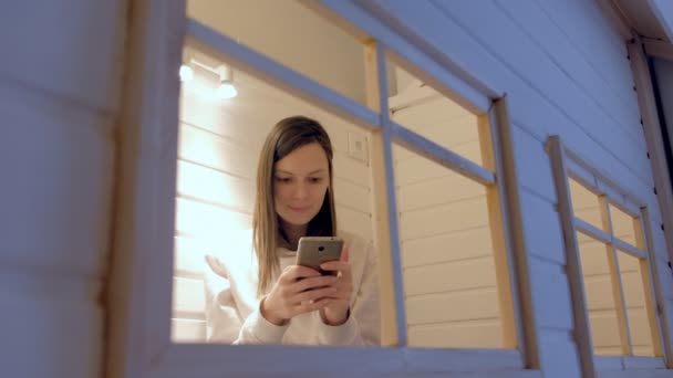 Woman types a message on phone sitting in kids play house, mom hiding from children. — Stock Video