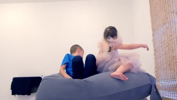 Broer en zus, meisje in een mooie jurk zit in een stoel-zak in de kinderkamer en spelen. — Stockvideo