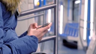 Kadın bir boş metro arabaya biniyor ve bir video onun smartphone üzerinde saatler. Yan görünüm, eller yakın çekim.