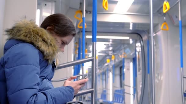 Kobieta jeździ w pustym samochodzie metra i ogląda film na swoim smartfonie. Widok z boku. — Wideo stockowe
