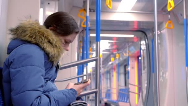 Woman rides in an empty subway car and watches a video on her smartphone. Side view. — Stock Video
