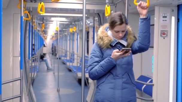 La mujer monta en un vagón de metro vacío y navega en su teléfono inteligente. Se para y sujeta la barandilla . — Vídeos de Stock