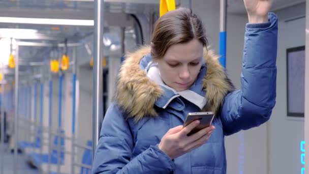 Retrato de mujer cansada monta en un vagón de metro vacío y navega en su teléfono inteligente. Se para y sujeta la barandilla . — Vídeo de stock